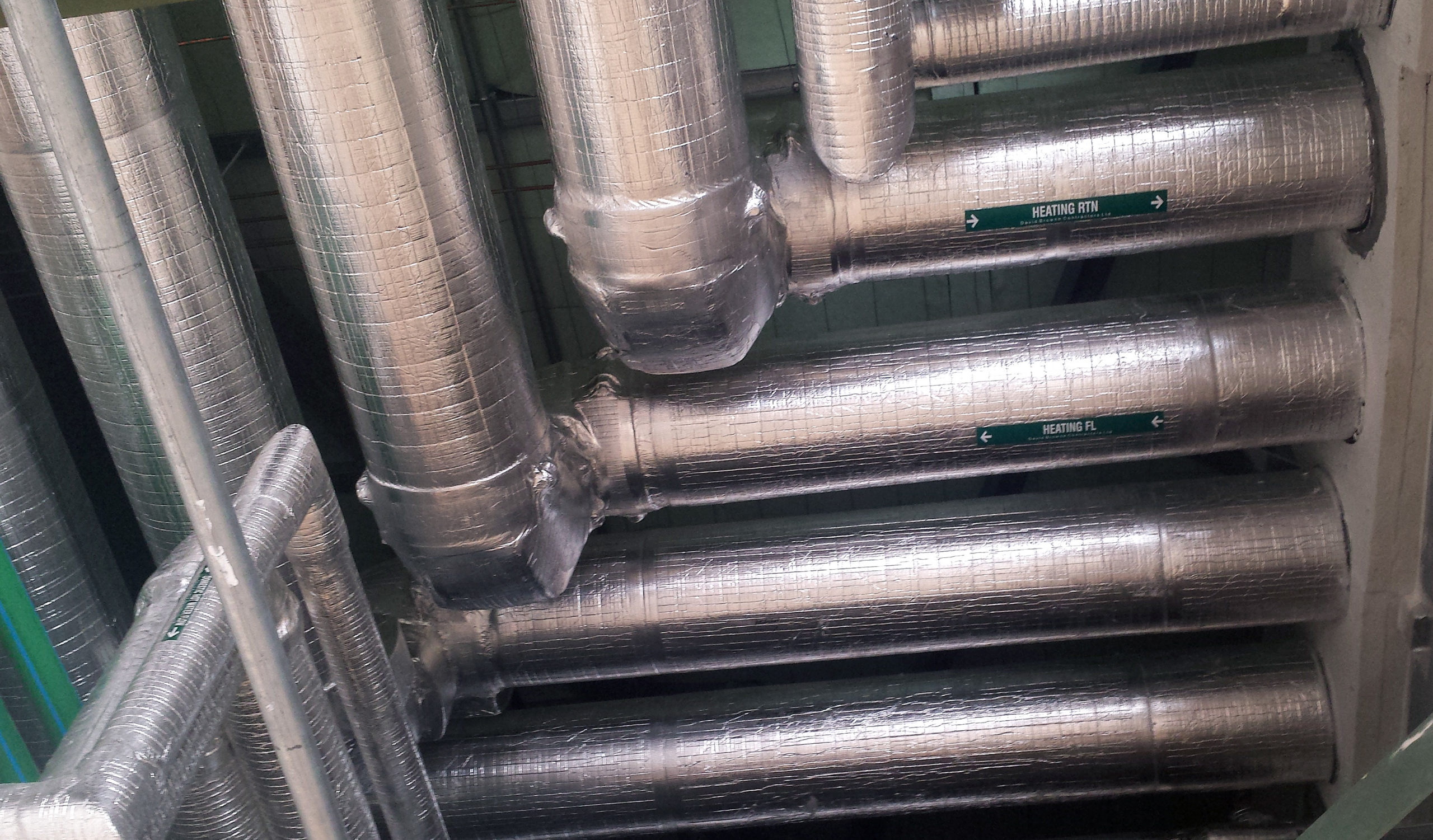 ภาพติดตั้งจริง Thermobreak LS ในห้องเครื่อง — เห็น label HEATING RTN/HEATING FL และ foil facing สีเงินหุ้มท่อ